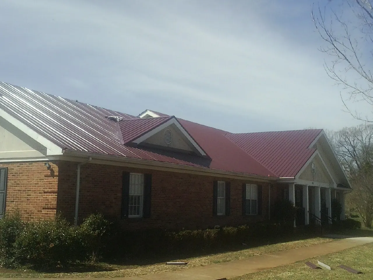 Red metal roof with gabled entries on a long brick building, from a Hail Damage Roof Repair job in Long Prairie