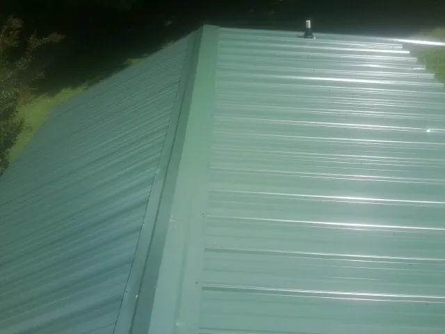 New green metal panels meeting at the ridge of a roof — Flat Roof Repair work by our crew in Long Prairie