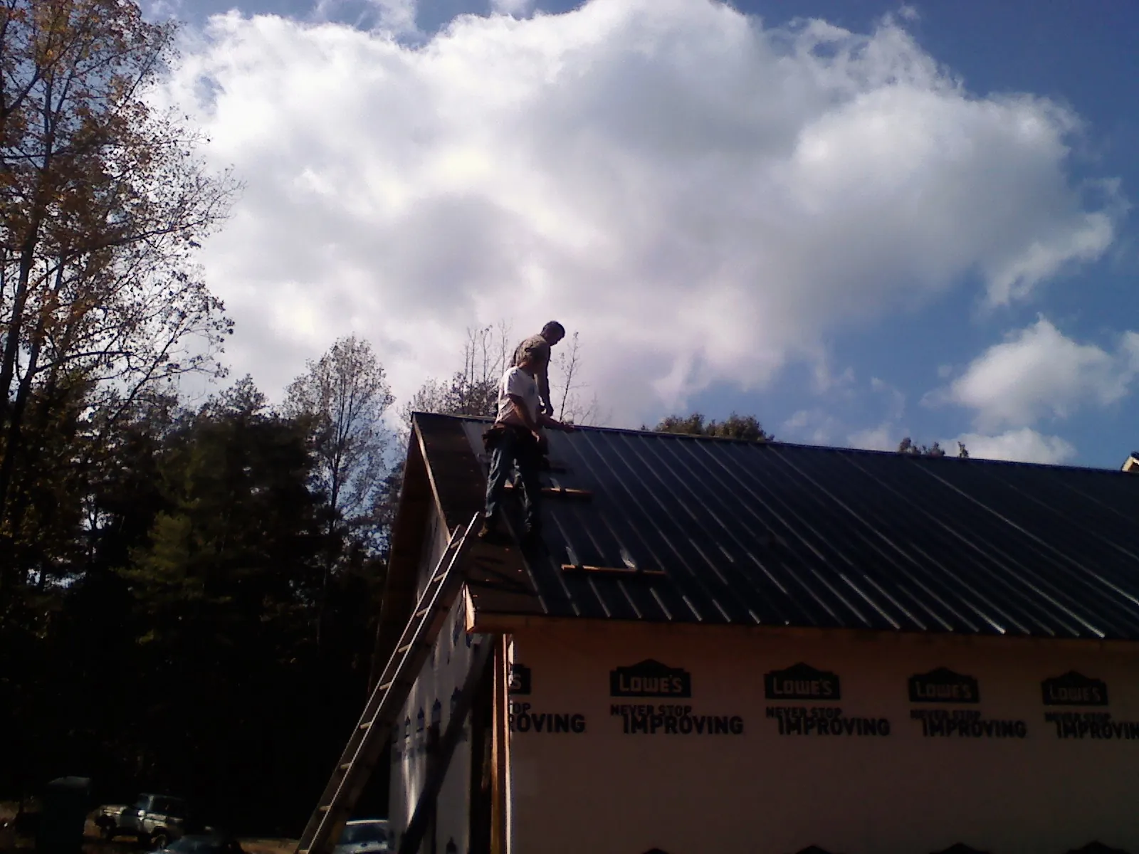 Roofer fastening dark metal panels high against a cloudy sky, from a Roof Inspection job in Long Prairie