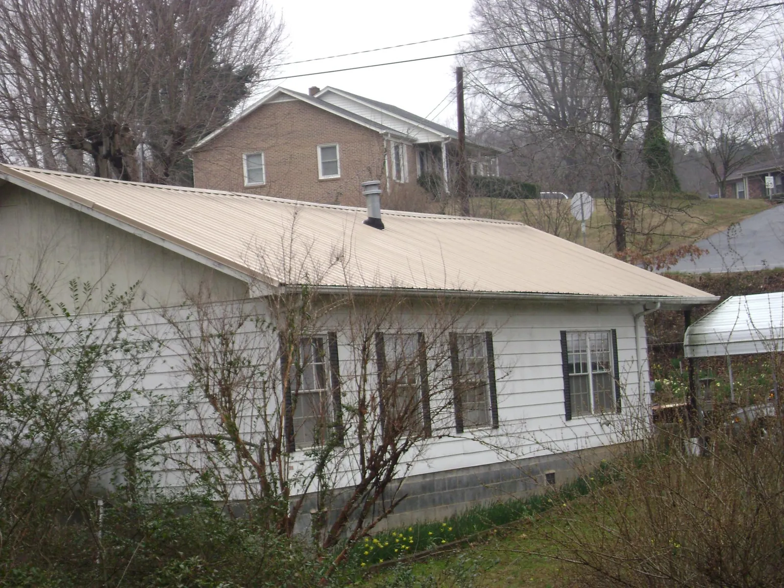 Tan metal roof on a white sided house set into a hillside — Commercial Roofing by Roofing Brothers in Long Prairie